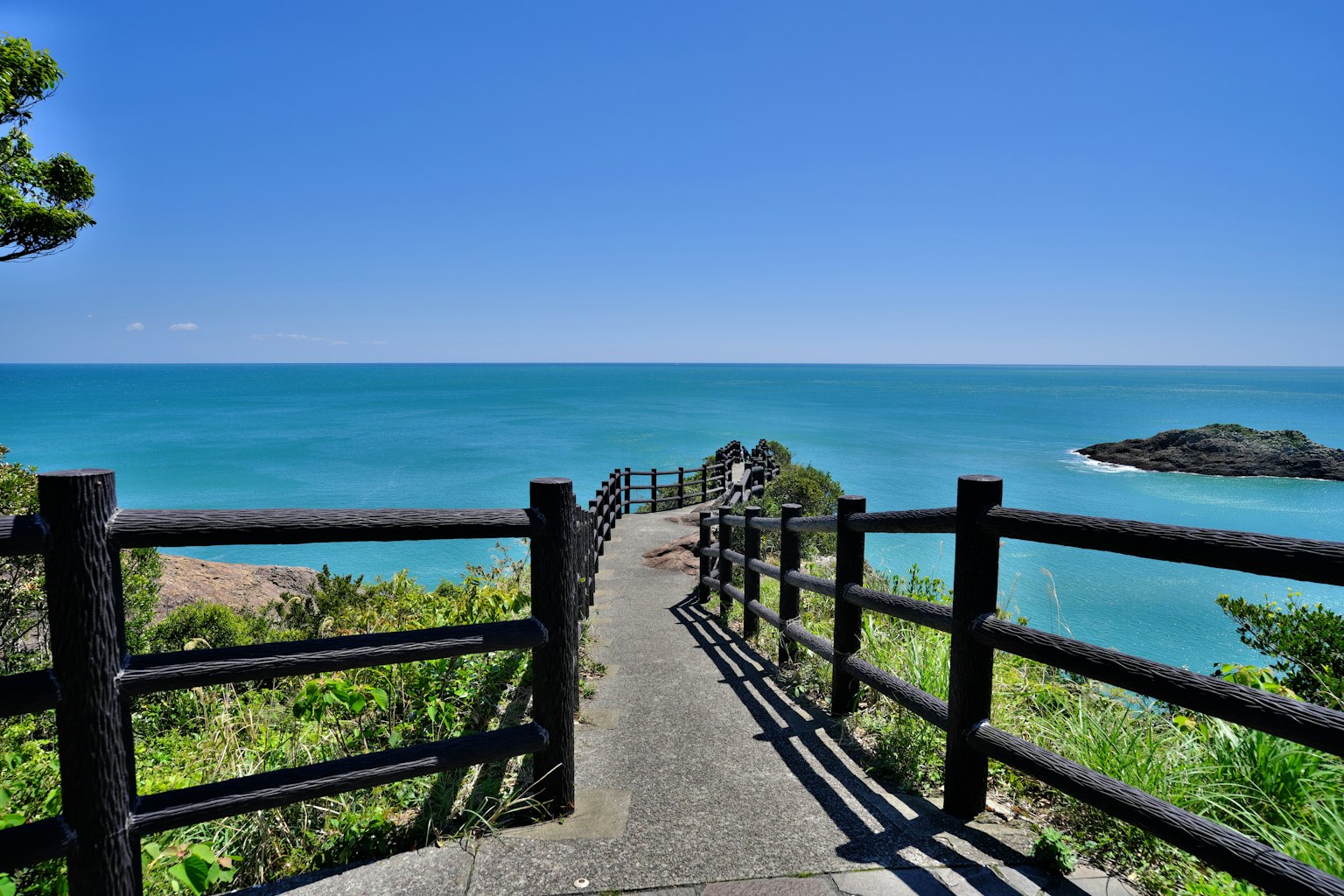 Weg mit Holzgeländer mit Blick auf das blaue Meer und den Himmel