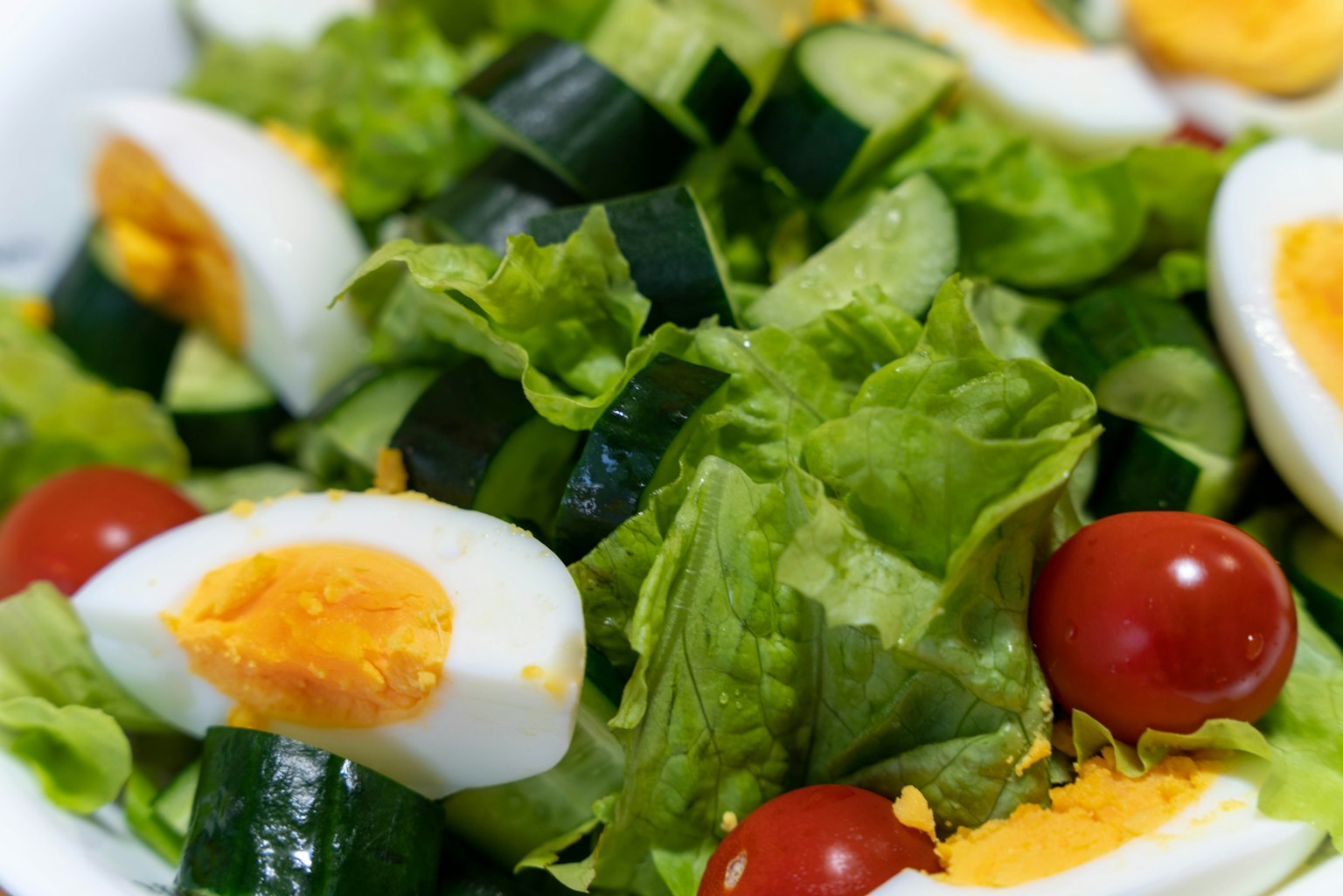 Un tazón de ensalada con lechuga, pepino, tomates cherry y huevos duros en rodajas