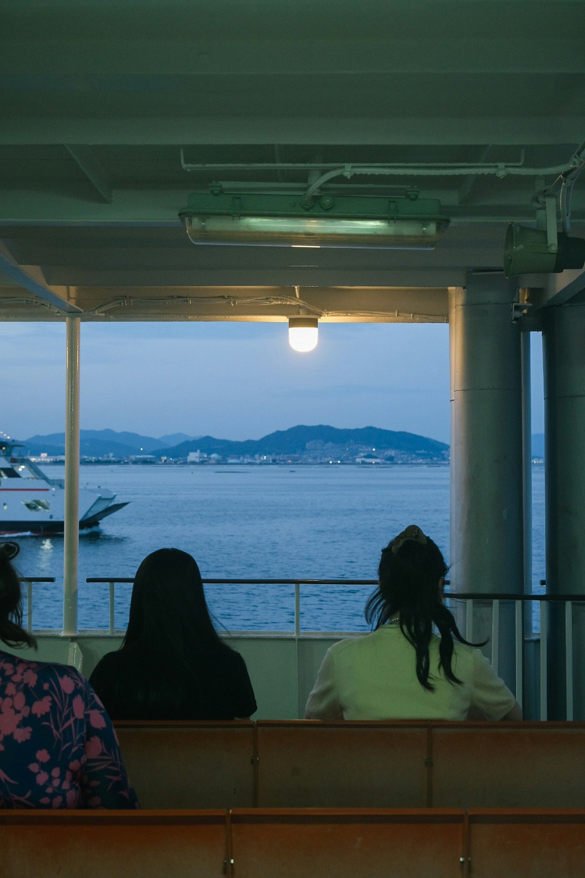 海を望む船内の窓辺で夕暮れの景色を眺める人たち