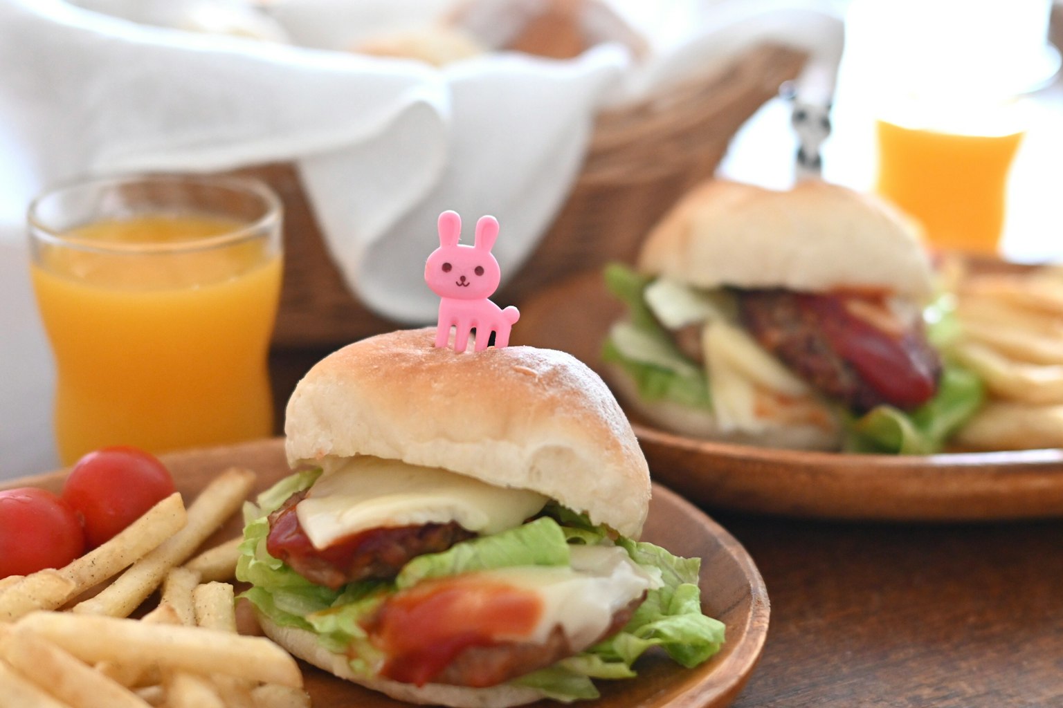 Hamburger colorato con lattuga e un topper a forma di coniglio rosa servito con patatine e succo d'arancia