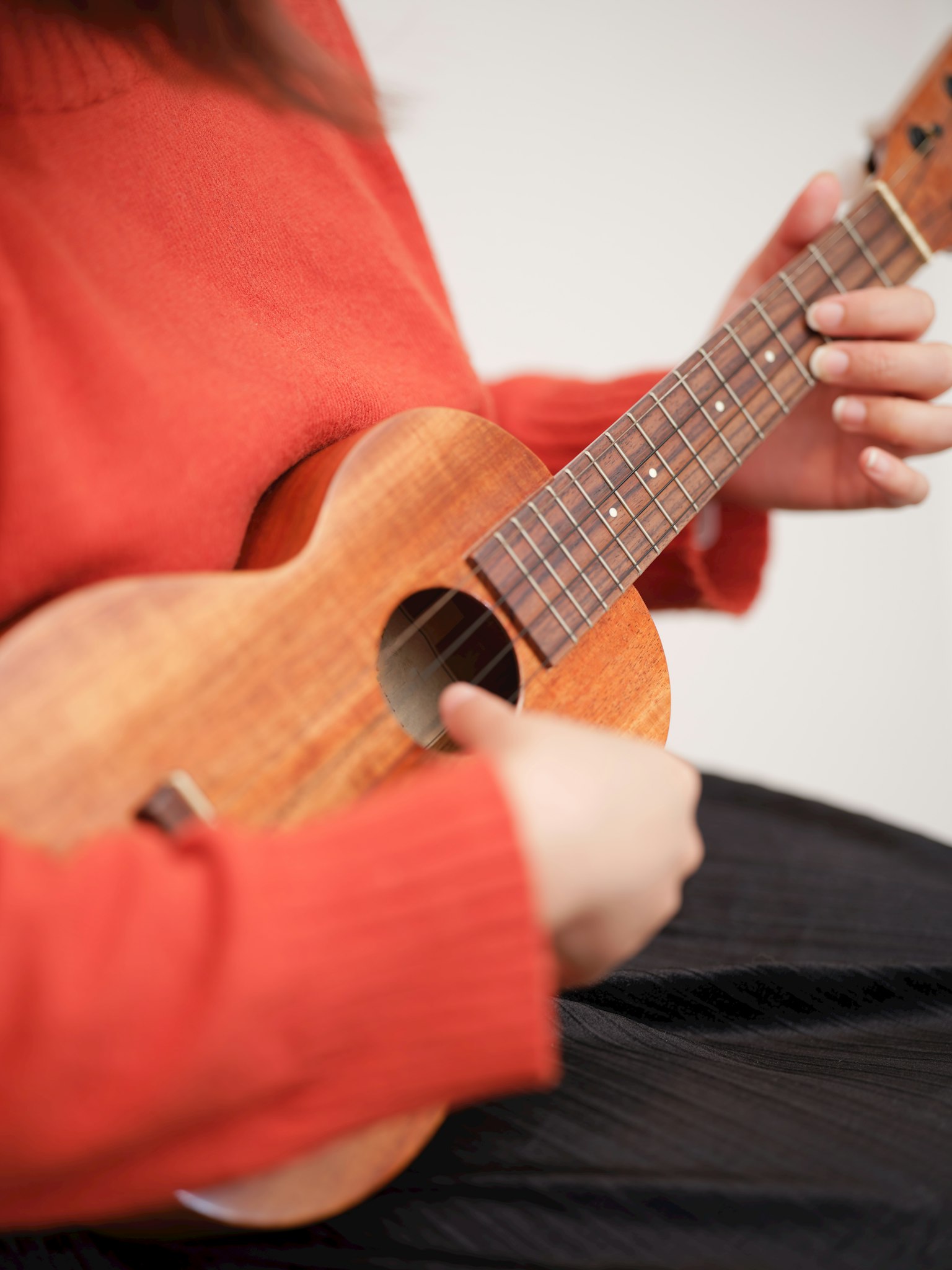 Cận cảnh bàn tay chơi ukulele với áo len màu cam ấm áp