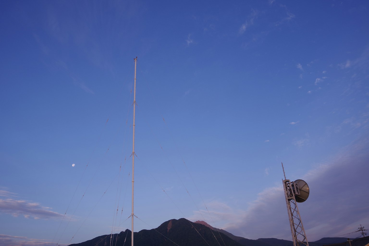 Hohe Kommunikationsantenne und kugelförmige Antenne vor blauem Himmel und Berg