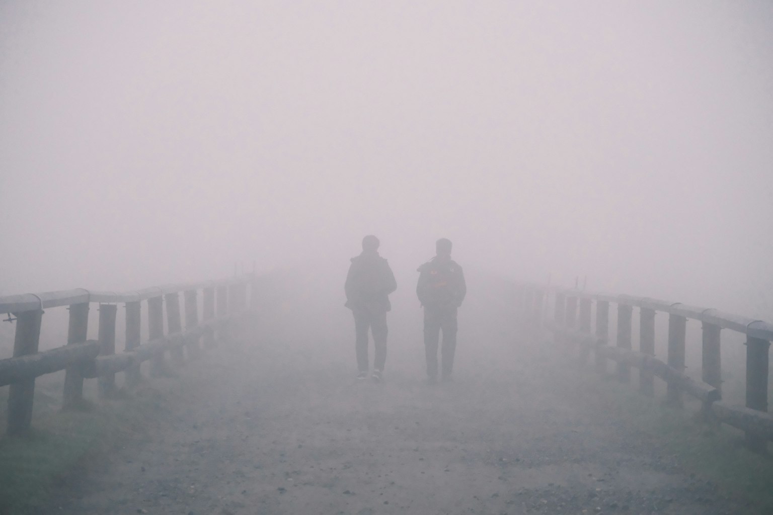霧の中を歩く二人の人物が見える橋の風景