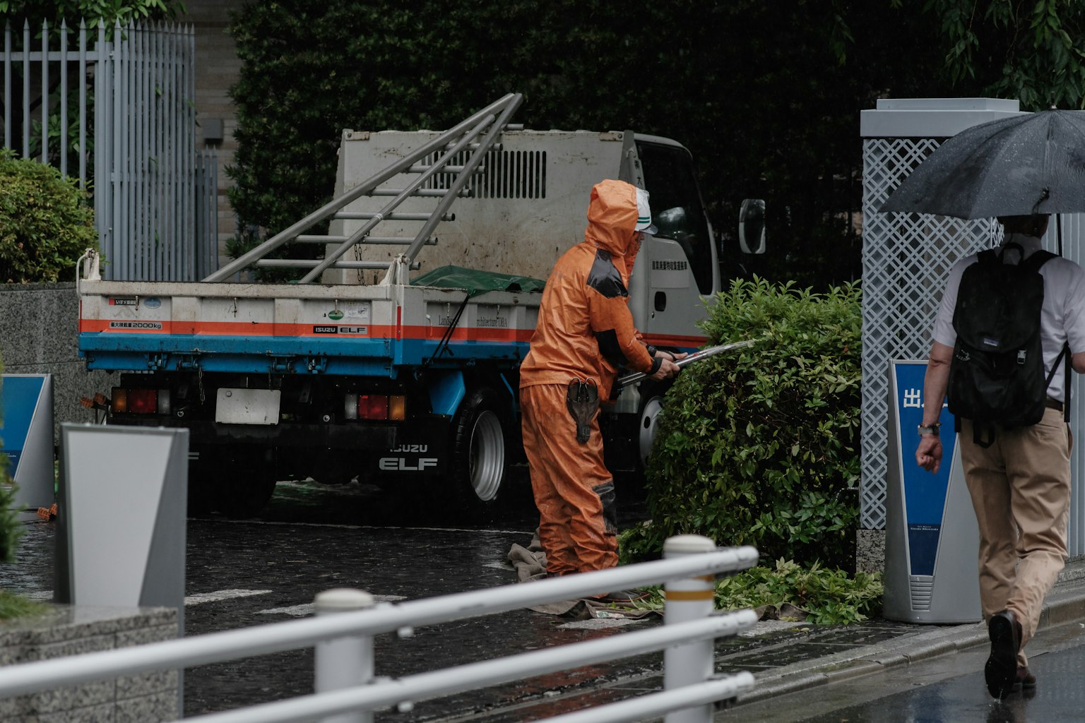 Un trabajador con uniforme naranja podando arbustos al lado de un camión