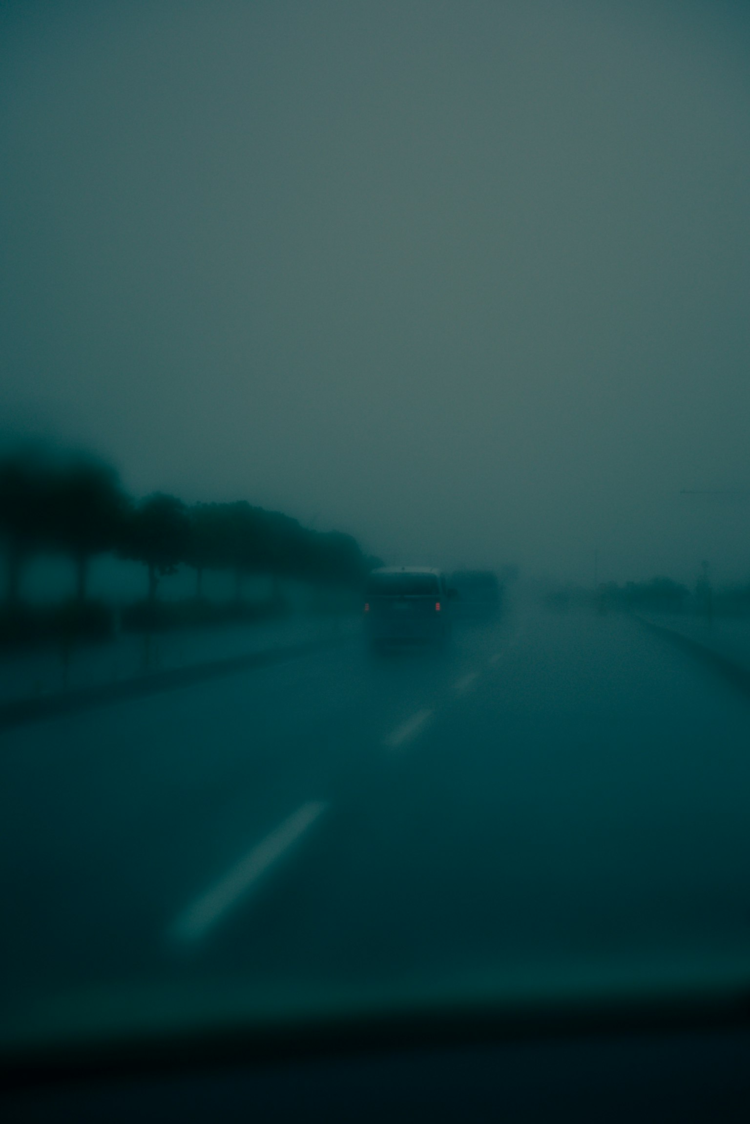 Verschwommene Sicht auf ein Auto, das auf einer regnerischen Straße mit Nebel fährt