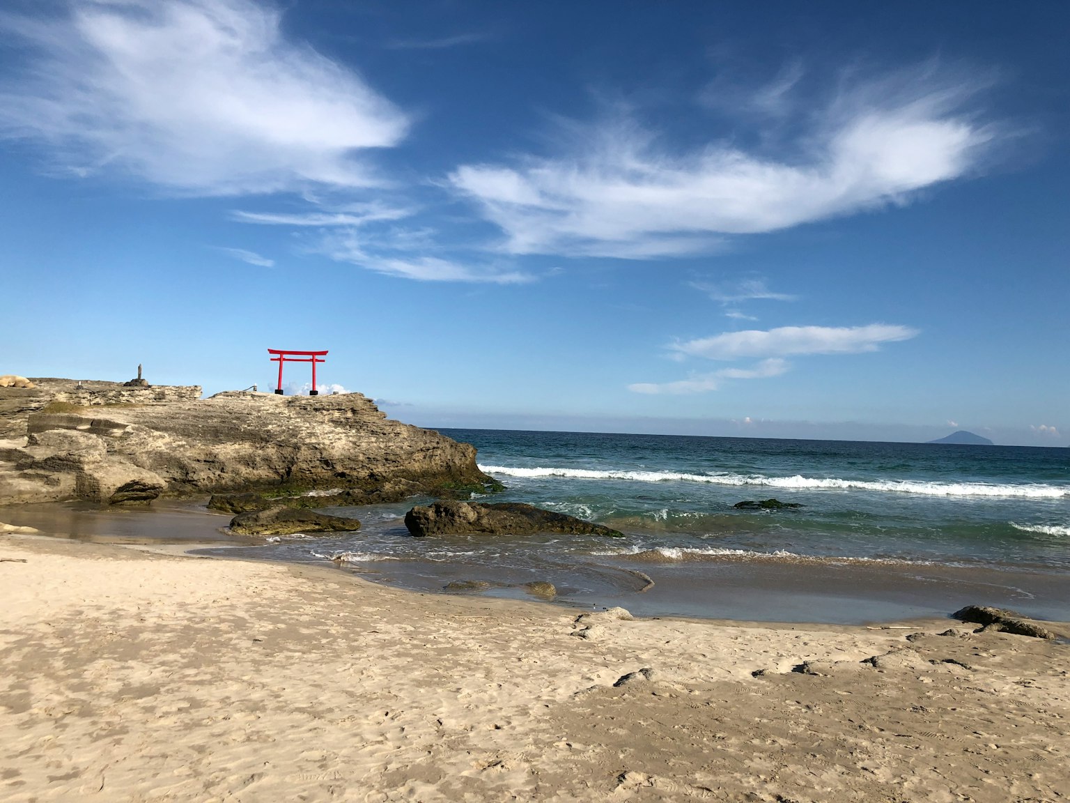 風景如畫的海灘景觀，藍色海洋和天空中有一個紅色鳥居