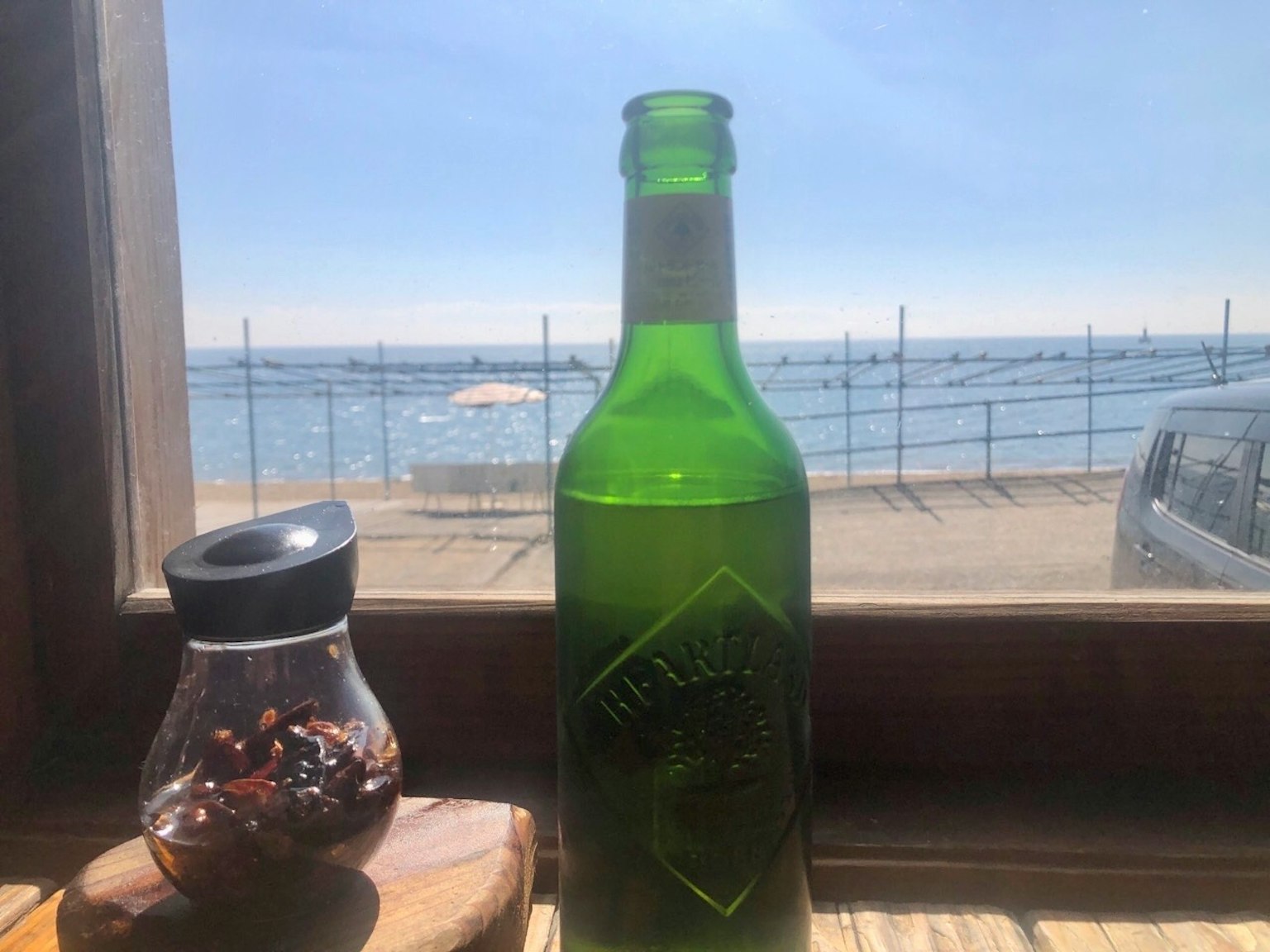 Une bouteille verte et un pot d'épices sur une table avec vue sur l'océan à travers la fenêtre