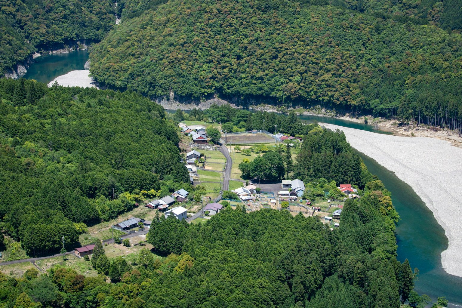 Aerial view of a small village surrounded by lush green mountains and a winding river