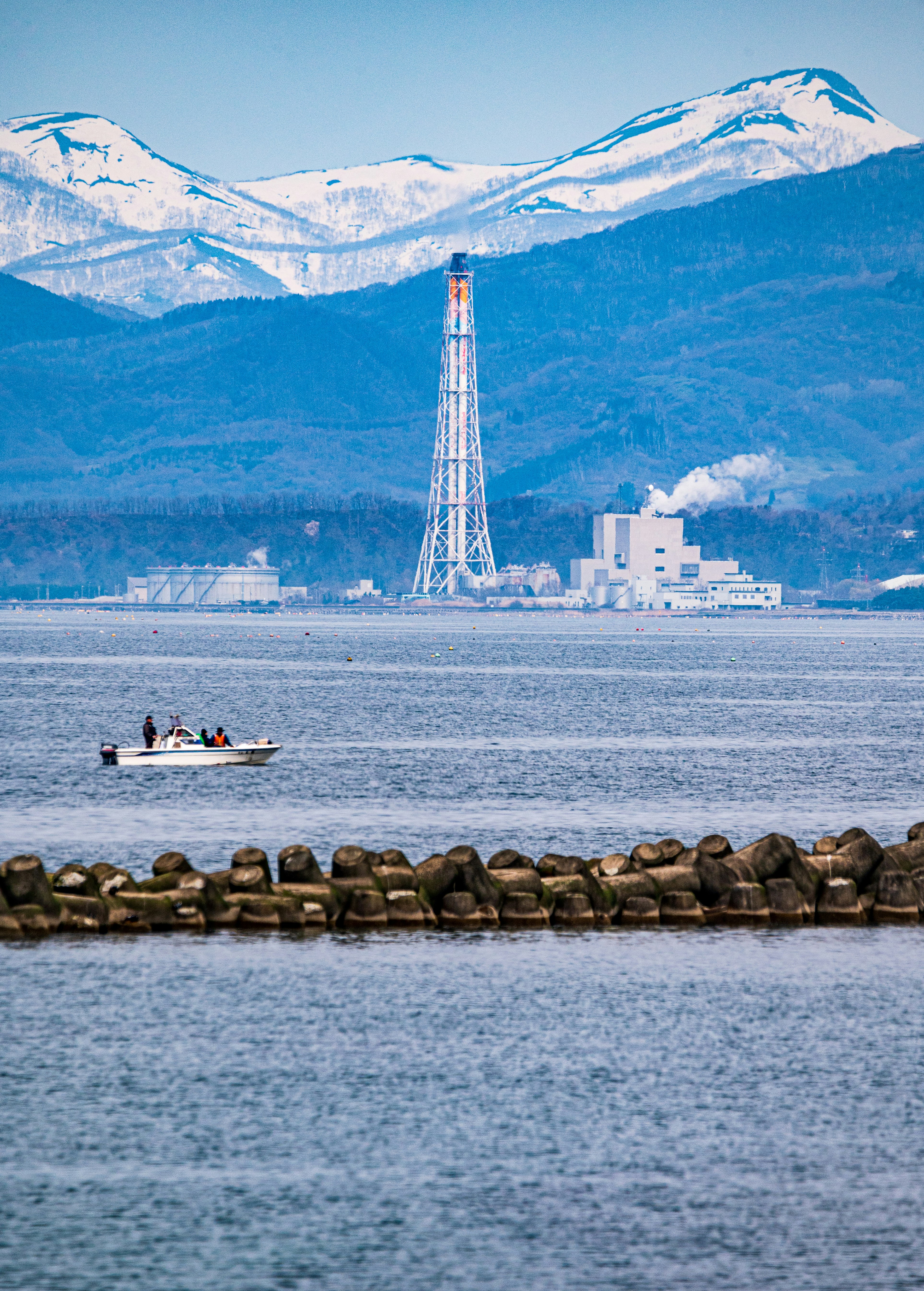 海边防波堤与船只，远处烟囱工厂与群山