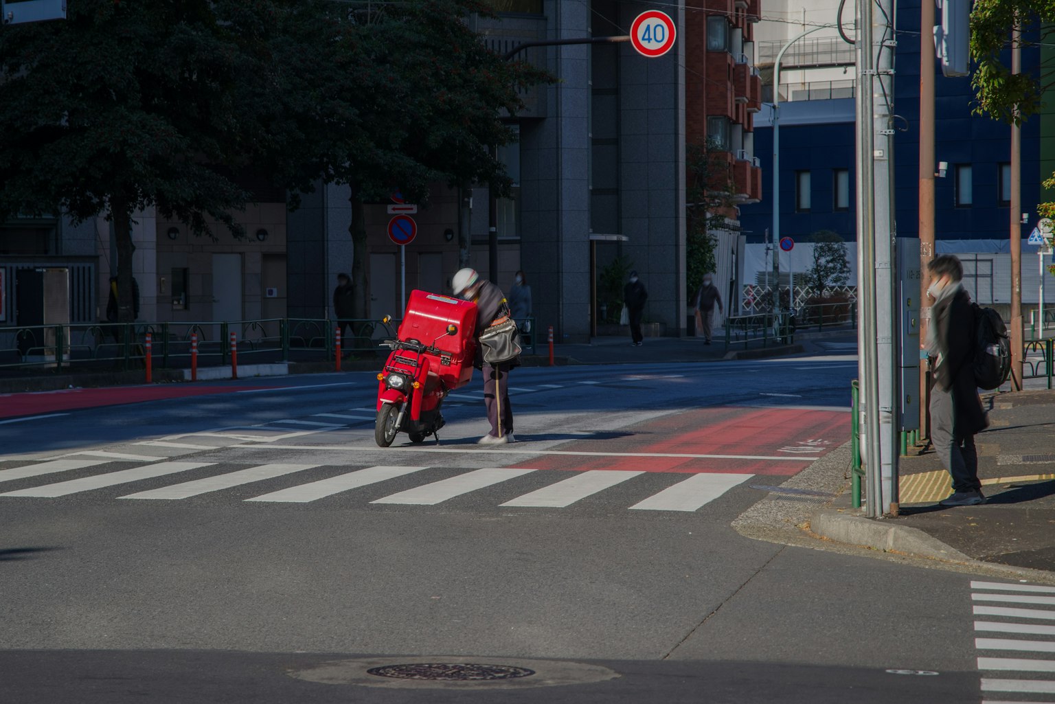 Un corriere su una moto rossa fermo a un attraversamento pedonale