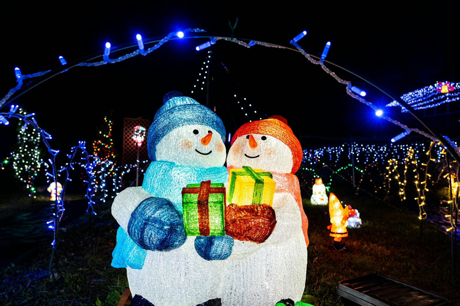 两个雪人手持礼物，周围是五彩缤纷的夜间灯光