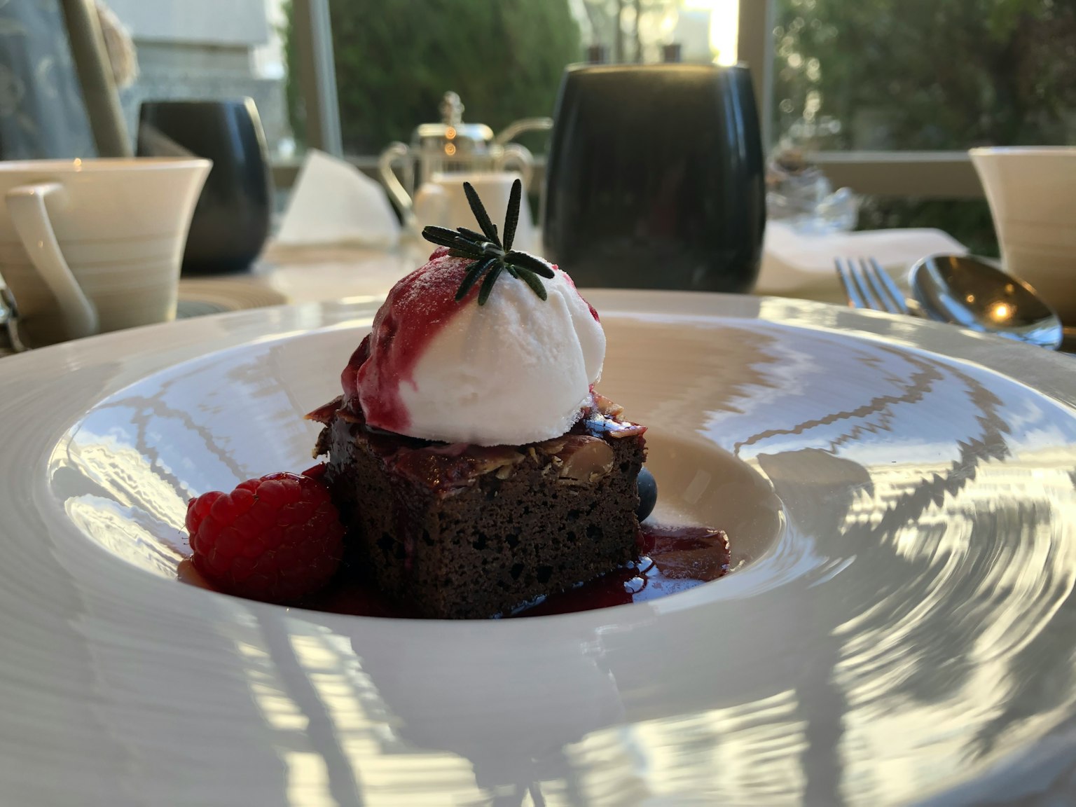 Piring makanan penutup yang disajikan dengan indah dengan kue cokelat di atasnya krim dan saus raspberry