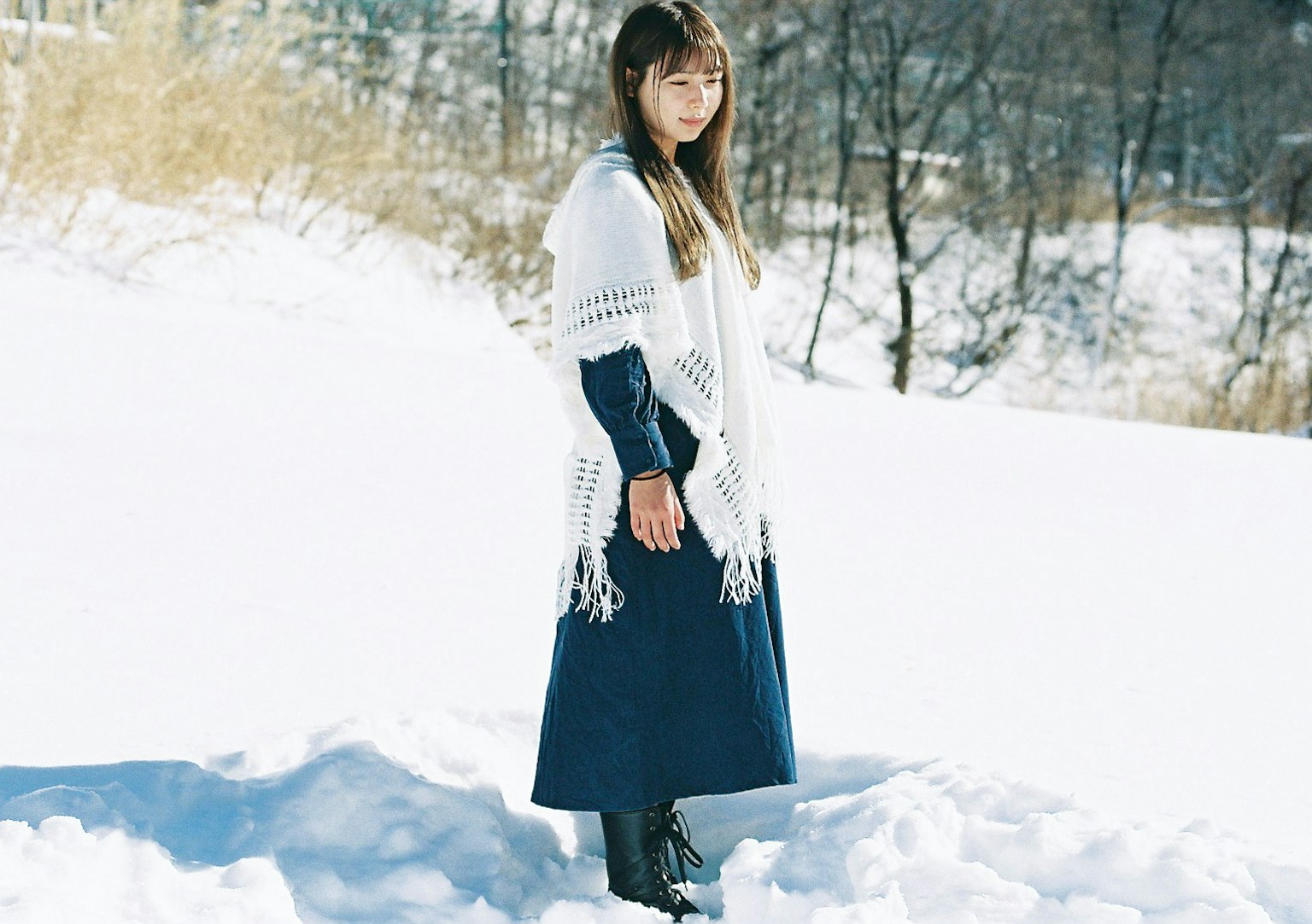 Una donna in piedi nella neve con un vestito blu scuro e un foulard bianco