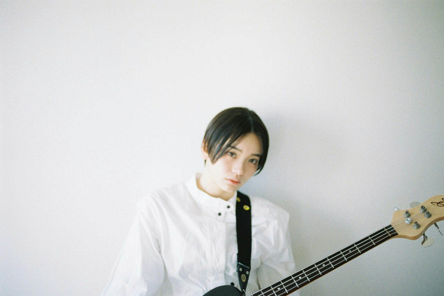 Retrato de una mujer sosteniendo una guitarra baja negra sobre un fondo blanco