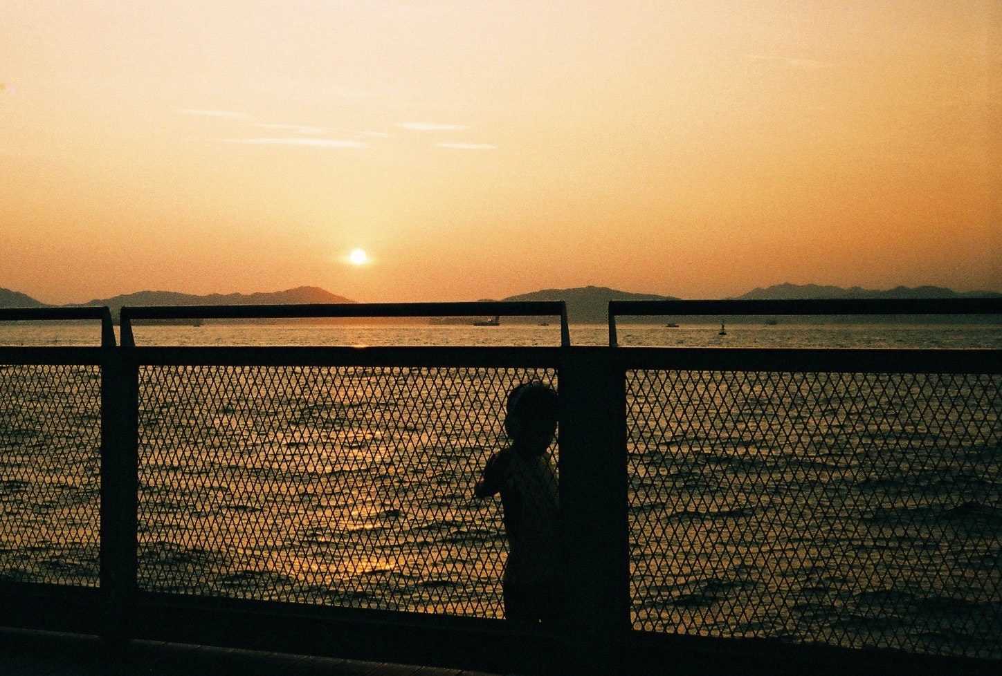 夕焼けの海辺を眺めるシルエットの人物