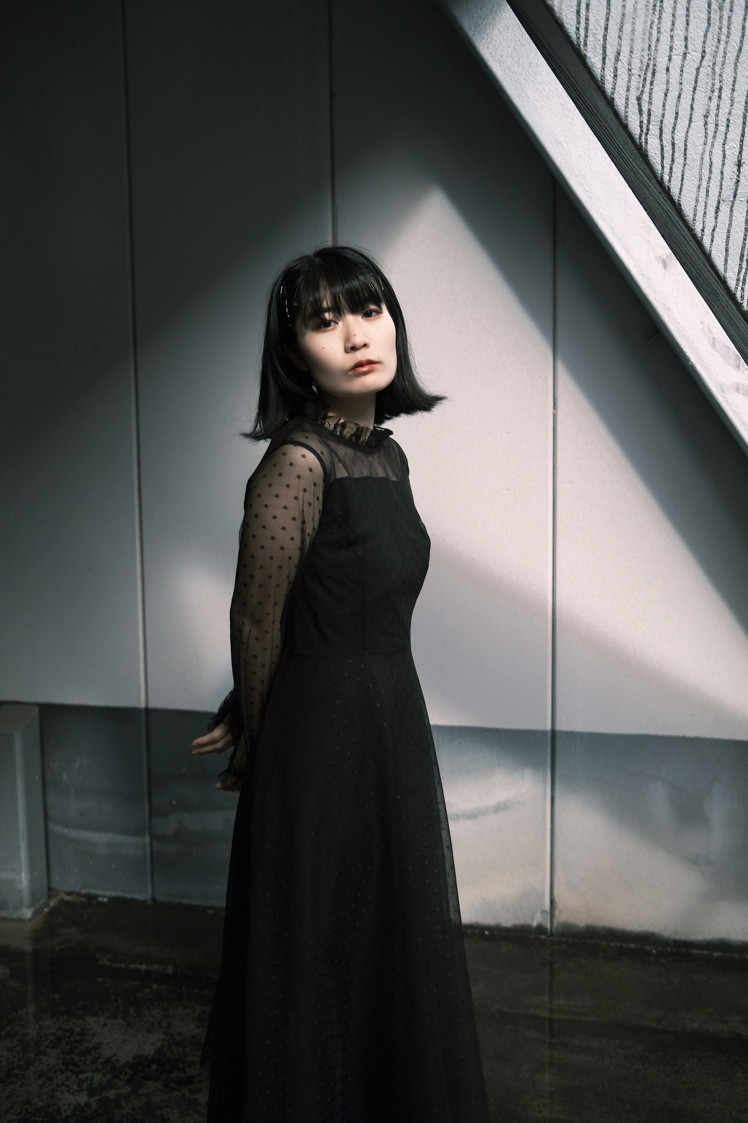 黒いドレスを着た女性が壁の前に立っている影のある写真