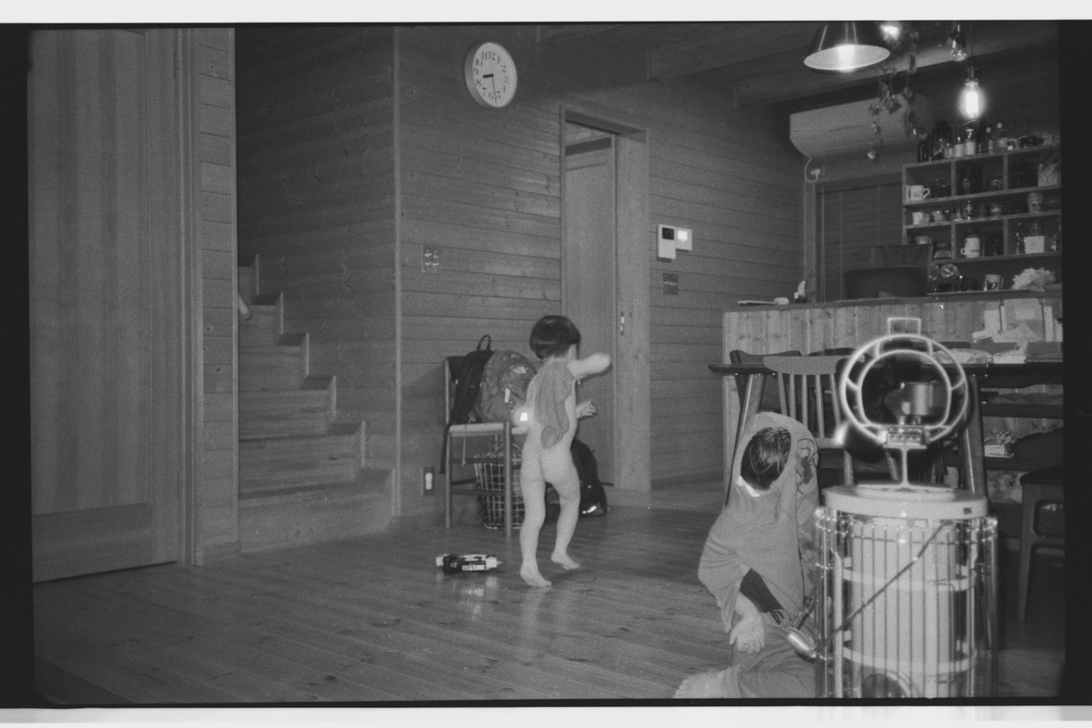 Bambino che gioca nudo in un ambiente domestico con orologio e scala visibili