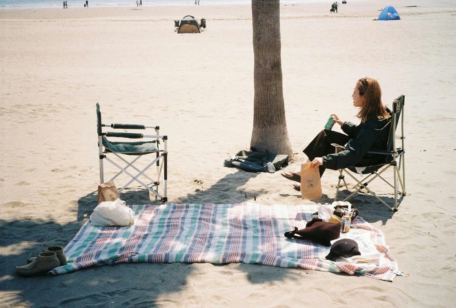 Eine Frau entspannt sich am Strand mit Stühlen Decke und einer Katze