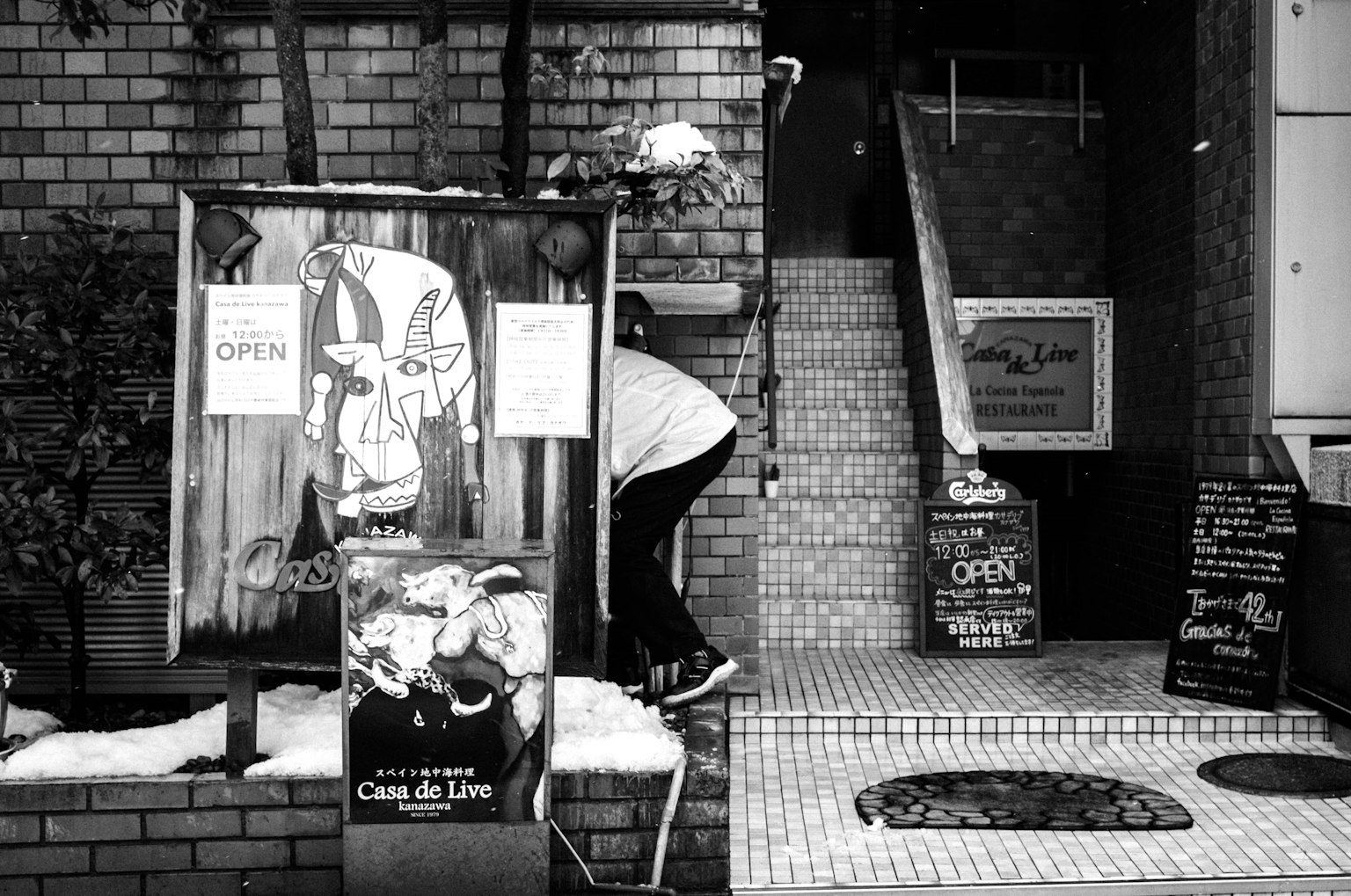 Extérieur en noir et blanc d'une entrée de magasin avec plusieurs panneaux affichés