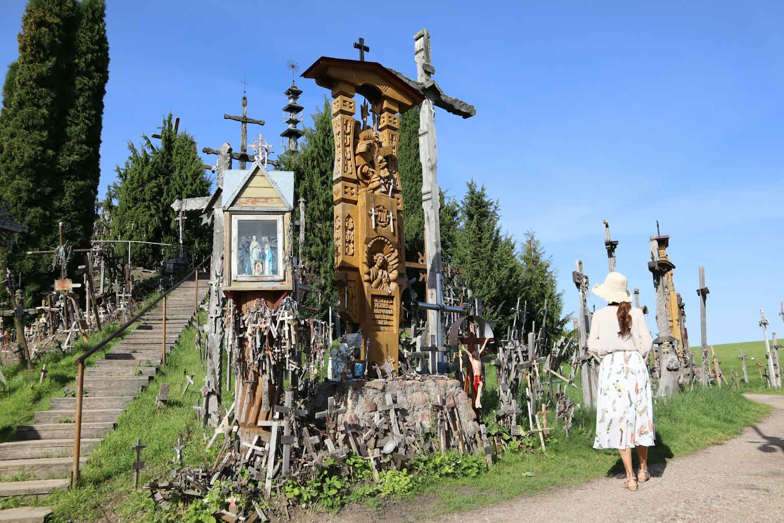 Una persona caminando junto a una colina adornada con cruces y esculturas de madera