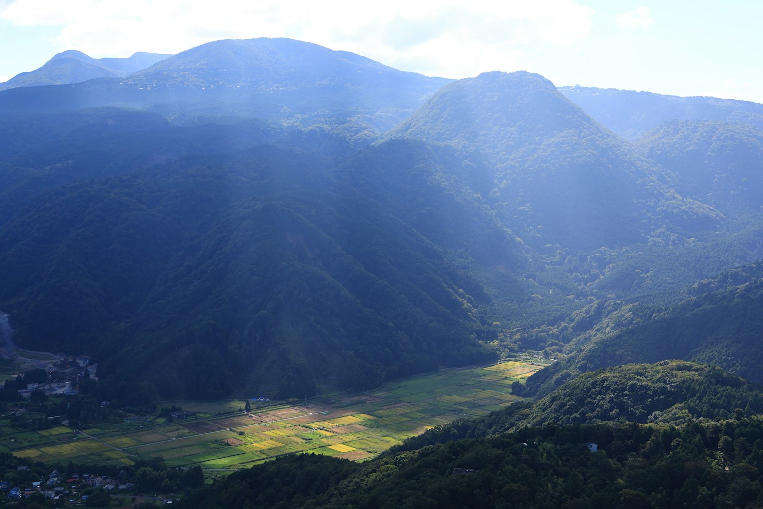 Luftaufnahme eines grünen Tals, umgeben von Bergen mit Sonnenstrahlen