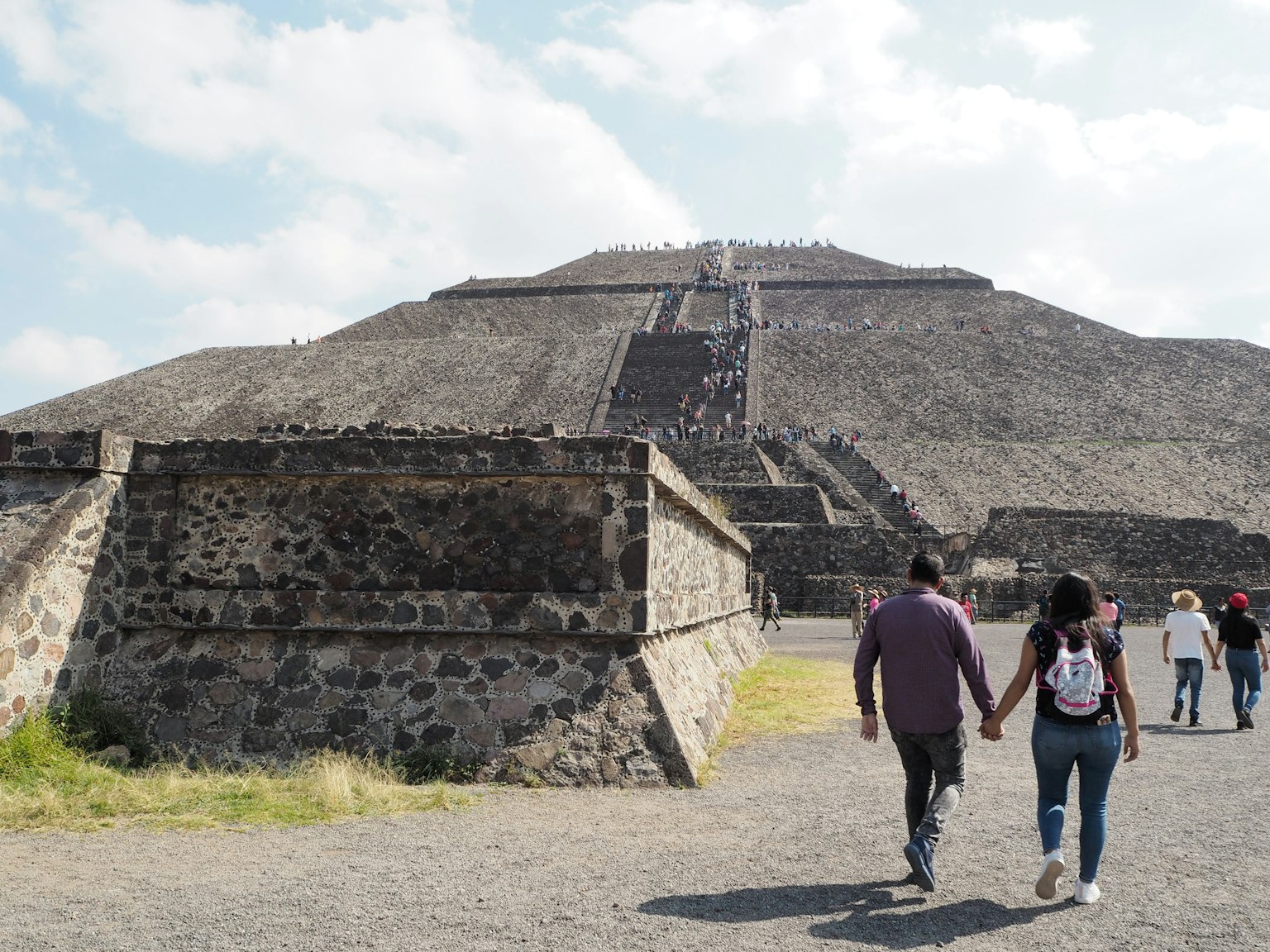 Paar, das Hand in Hand mit der Sonnenpyramide in Teotihuacan im Hintergrund geht