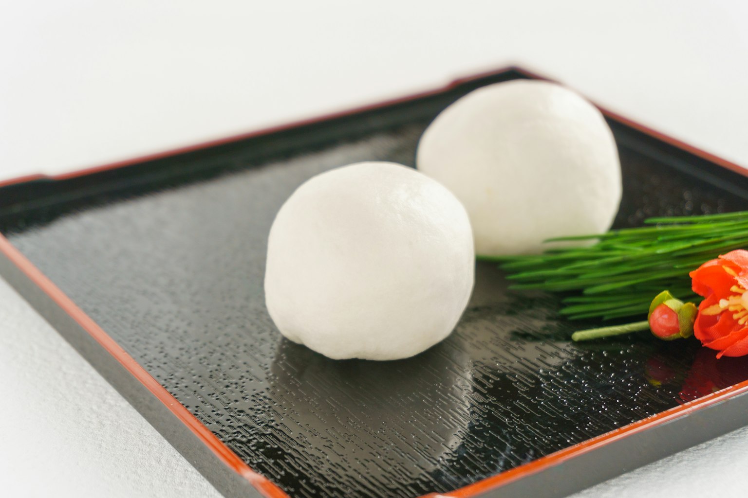 Dos bolitas blancas sobre un plato negro con cebollino y flores naranjas
