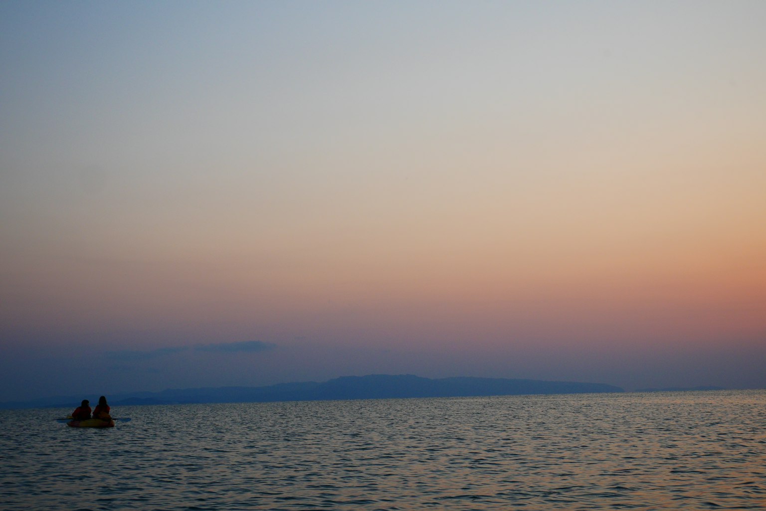 Un coucher de soleil serein sur l'océan avec un petit bateau au loin