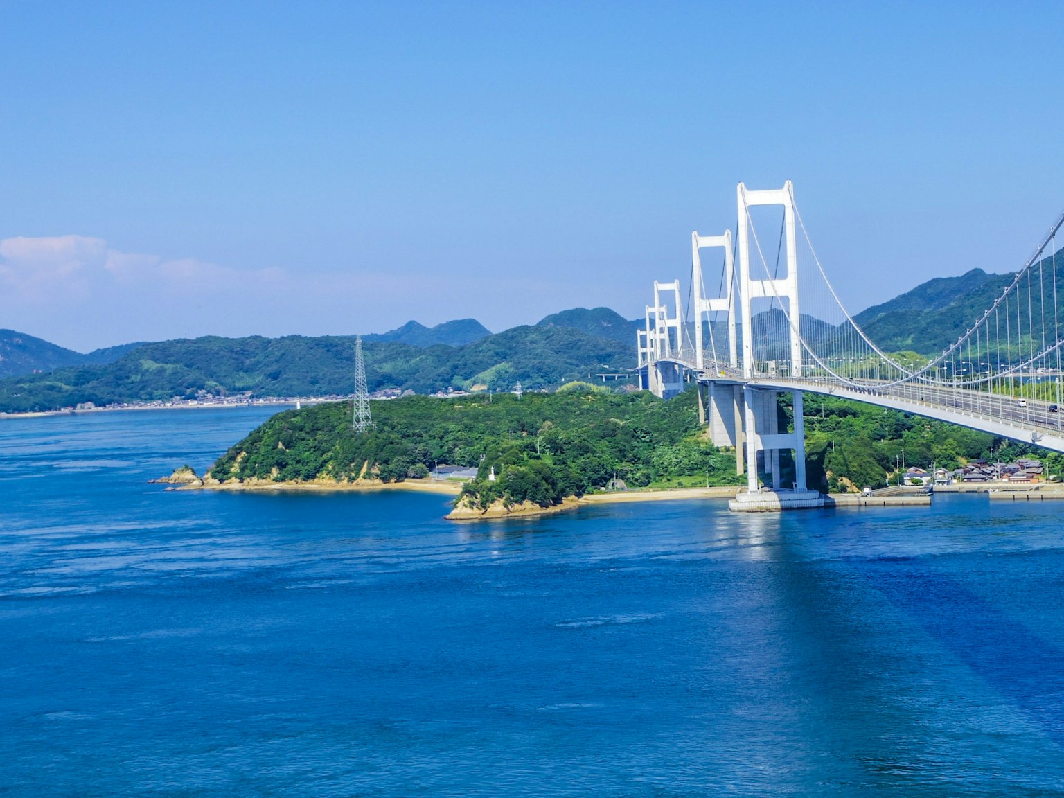 Vista panoramica di un ponte che si estende su acque blu con colline verdi sullo sfondo