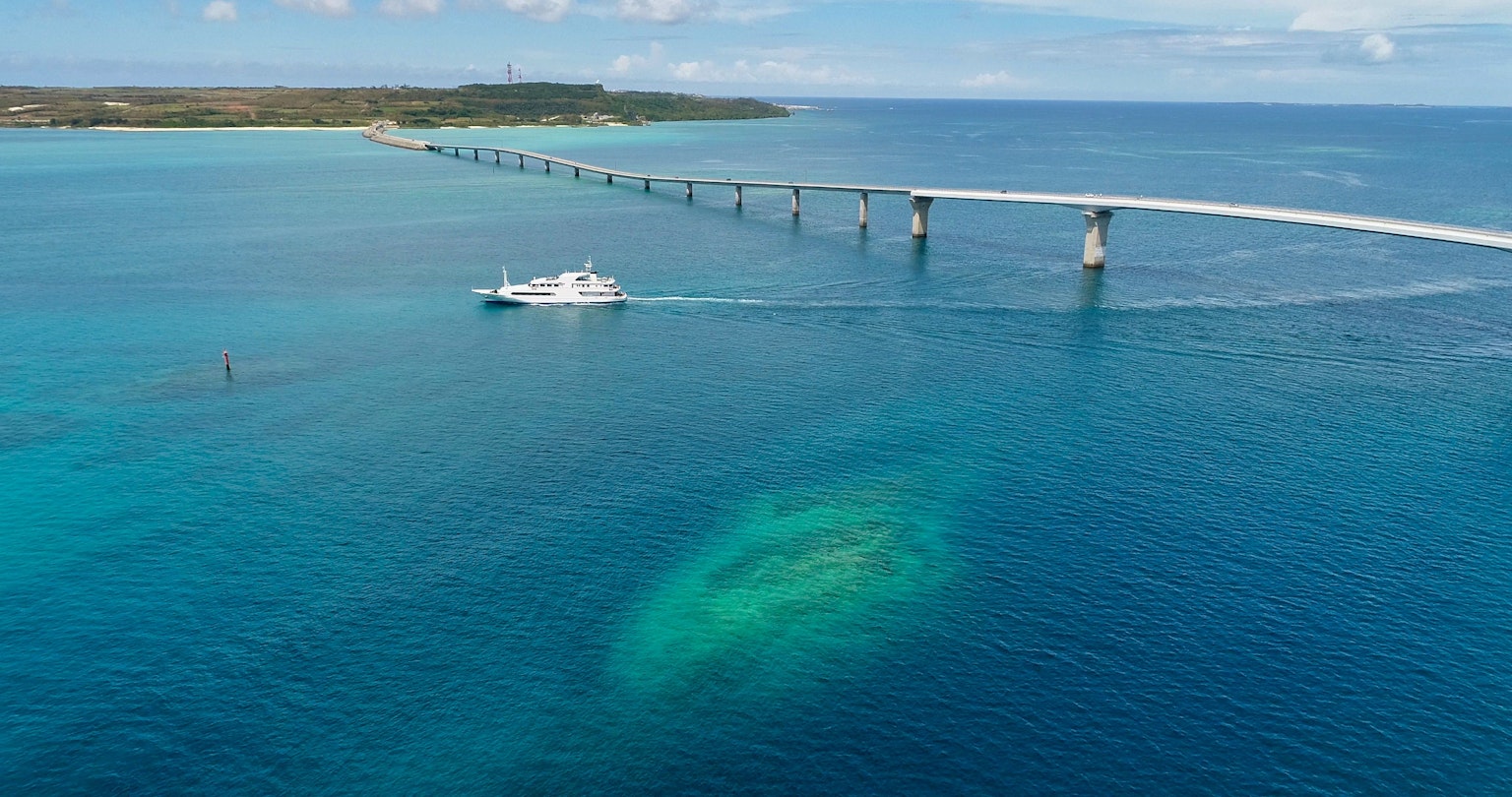 A boat cruising in the blue sea near a bridge