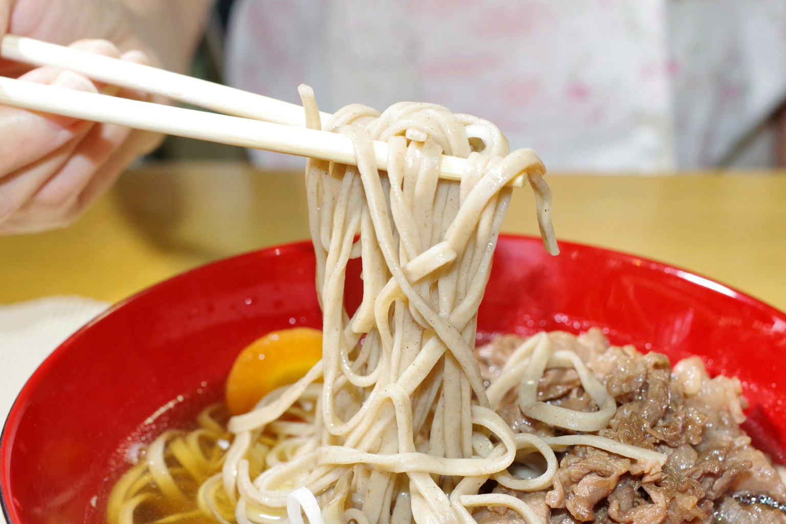 Une main soulevant des nouilles soba d'un bol rouge