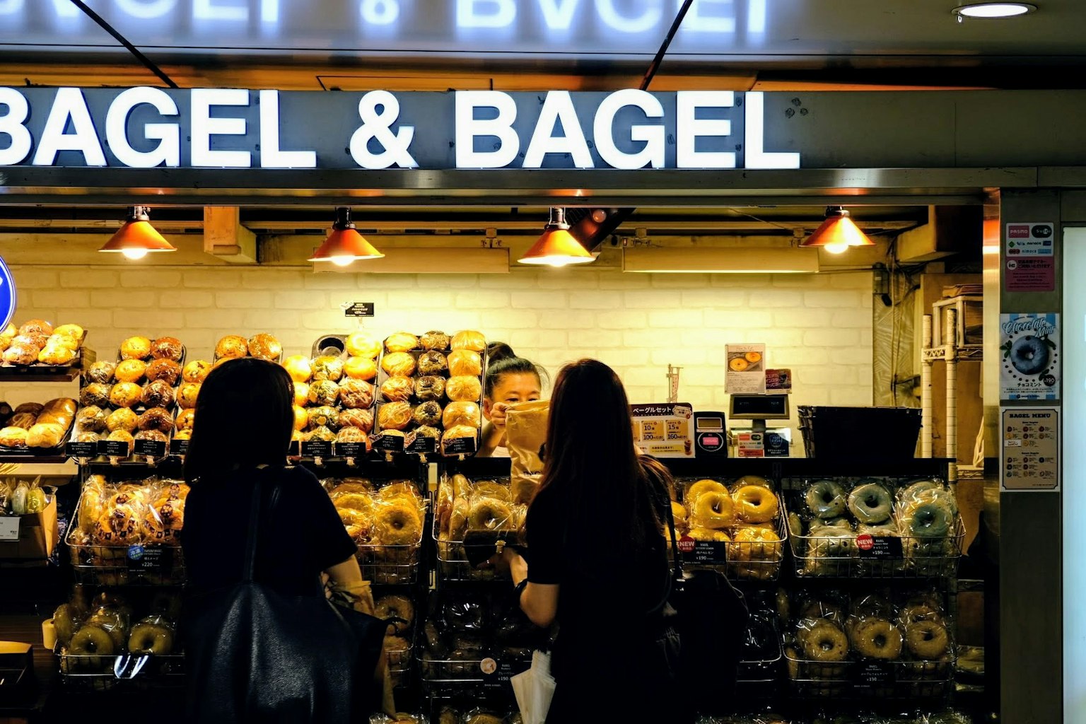 Two women in black clothing observing bagels at a Bagel & Bagel store
