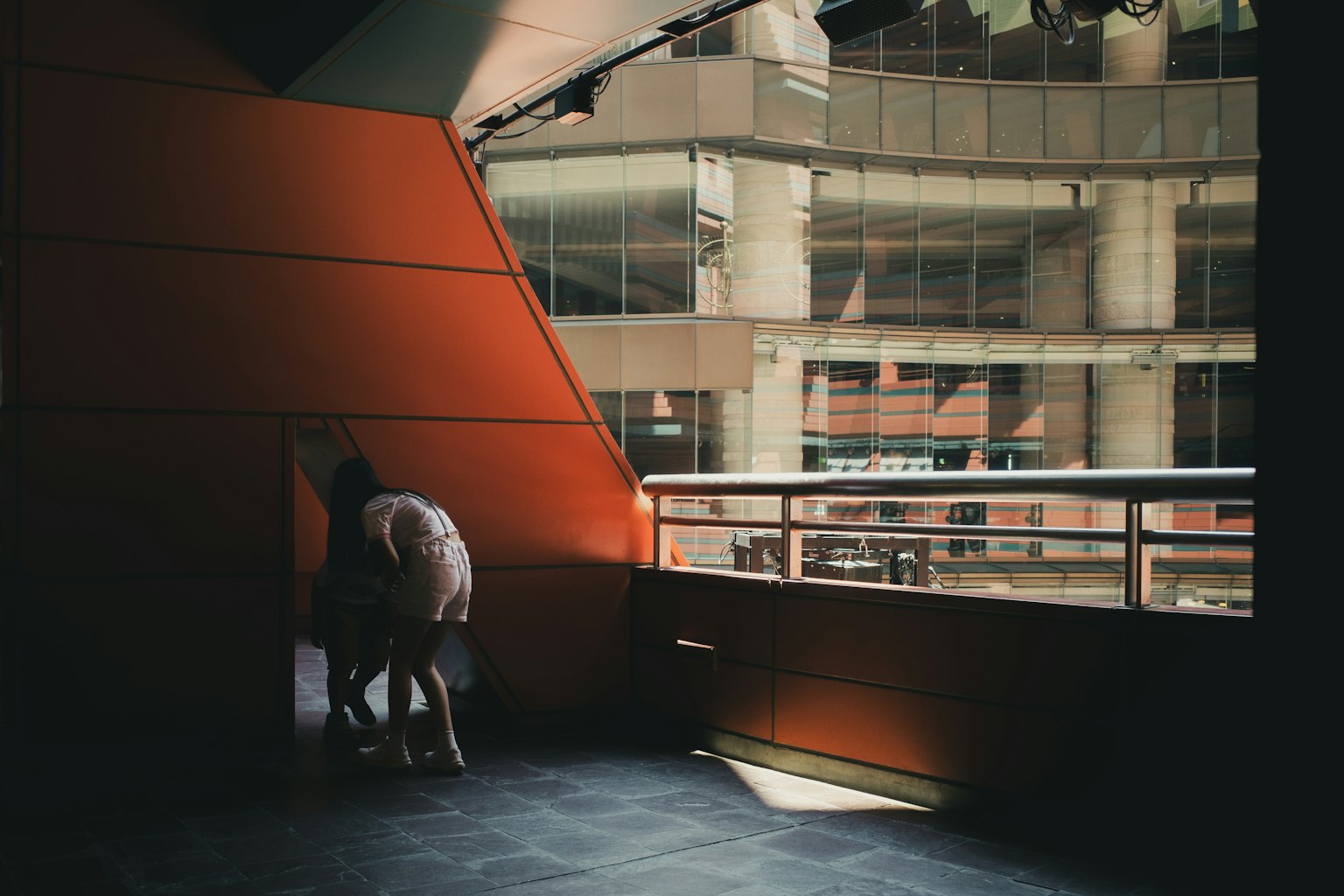 Interior de un edificio moderno con una pared naranja y un balcón de vidrio con personas reunidas