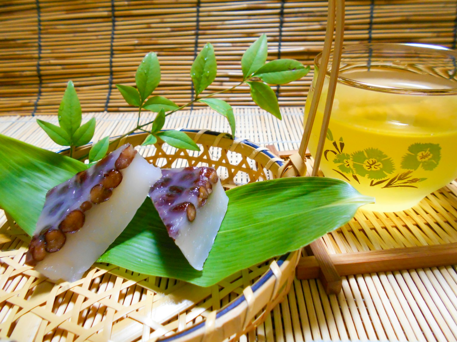 Japanese sweets placed on green leaves with a glass of green tea