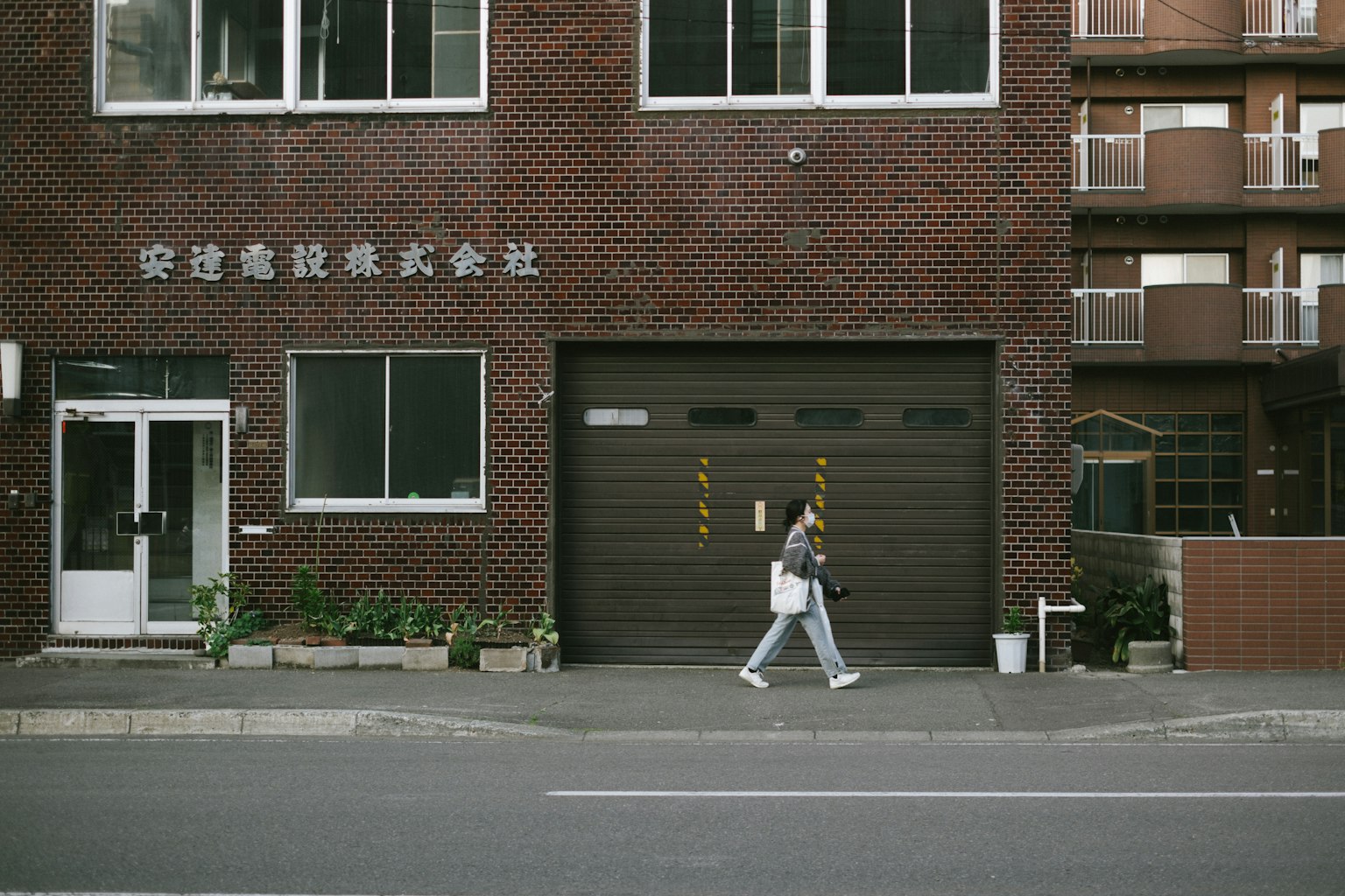 一名女性走在砖砌建筑前，旁边有植物