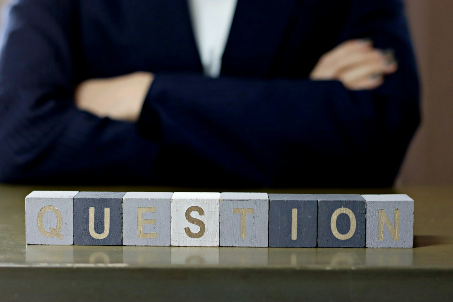 คำว่า 'QUESTION' ที่ทำจากบล็อกวางอยู่หน้าคนในชุดสูทสีเข้ม
