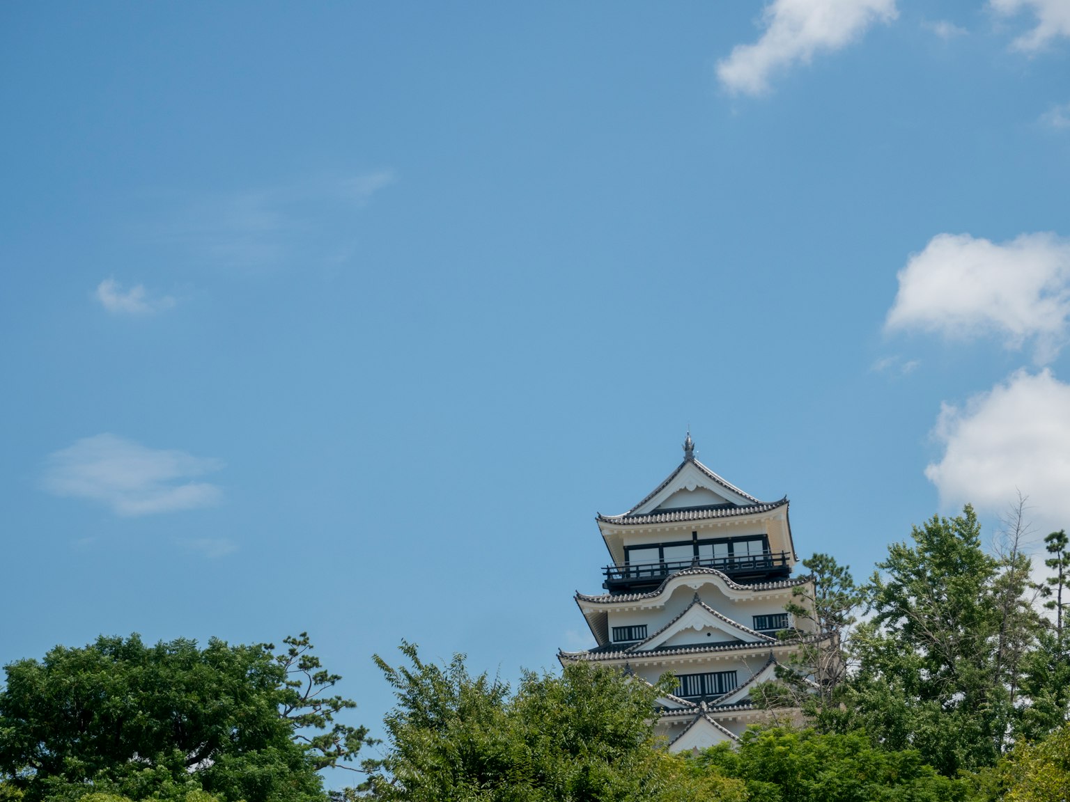 White castle tower rising under a blue sky with green trees