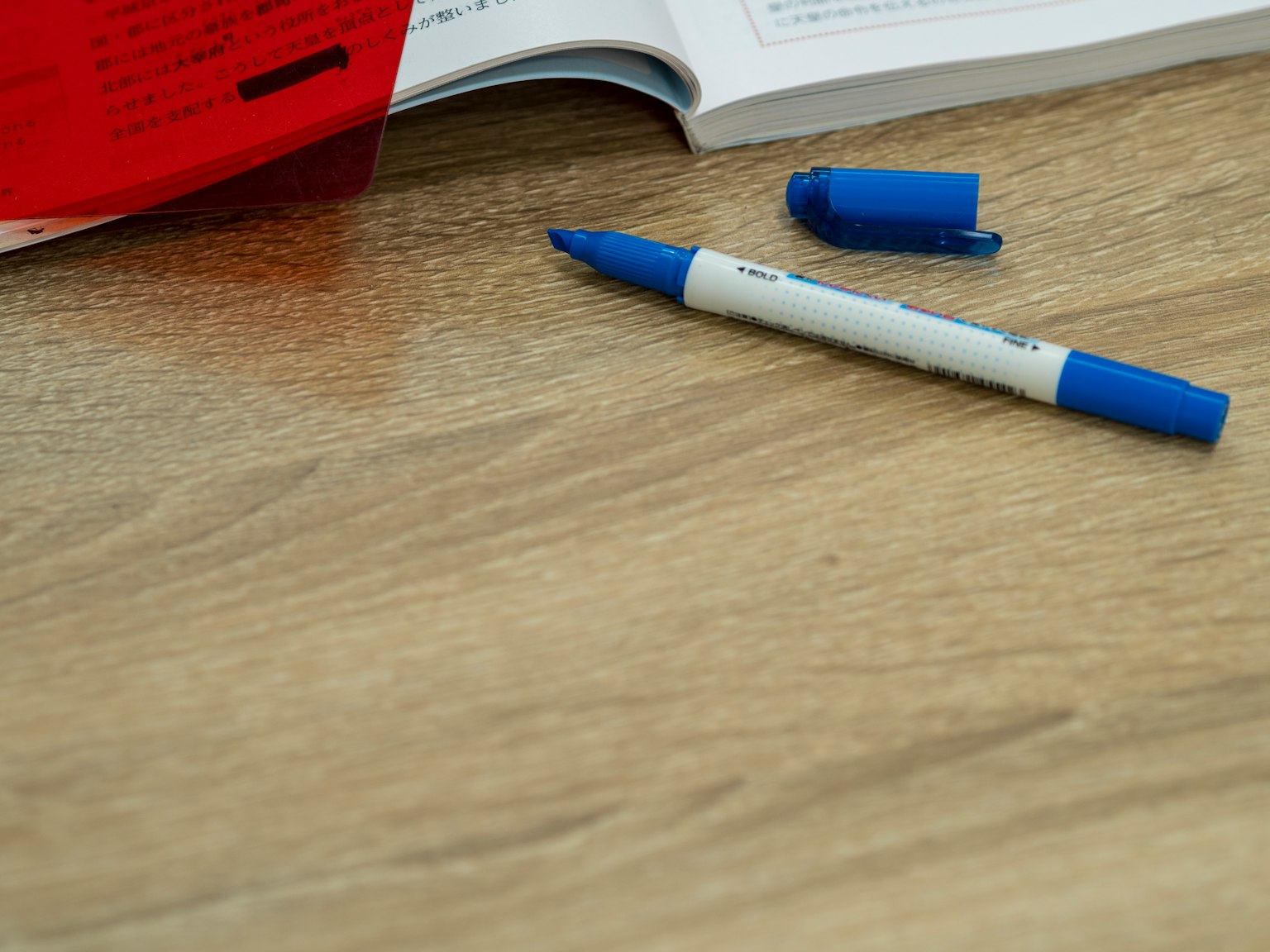 Un bolígrafo azul y una cubierta roja están sobre un libro colocado en una mesa de madera