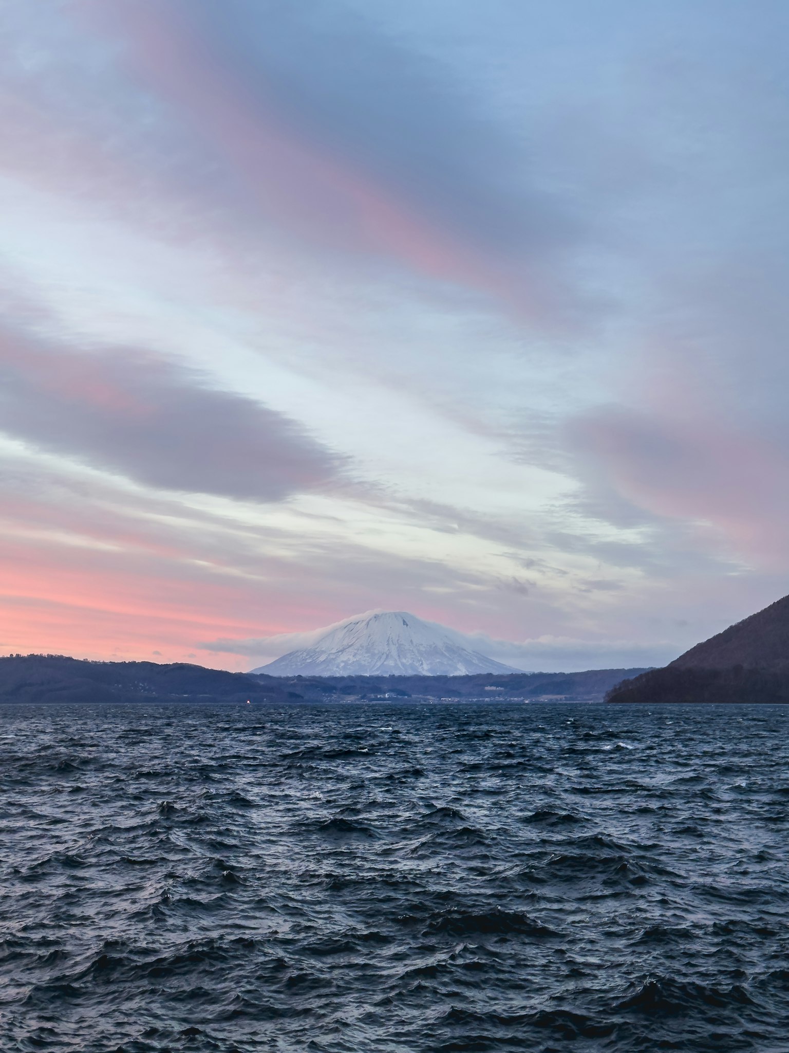 Pemandangan indah laut tenang di bawah langit senja yang berwarna-warni dengan gunung bersalju di kejauhan