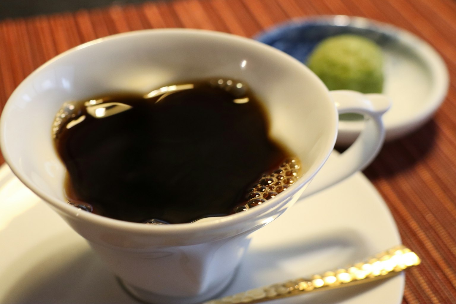 白色杯子裡的濃黑咖啡，旁邊是綠茶點心
