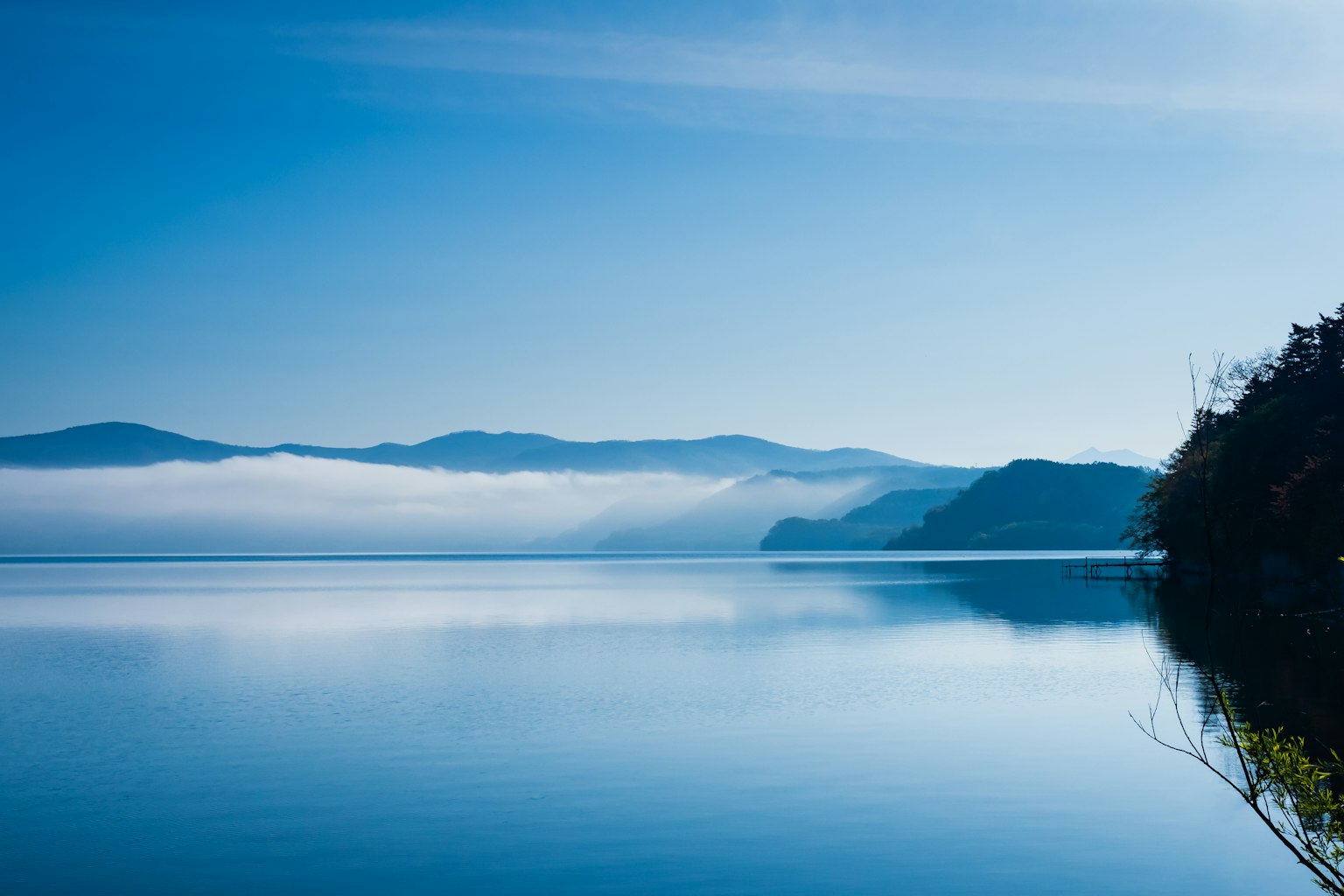 Pemandangan danau biru dengan pegunungan berkabut di latar belakang