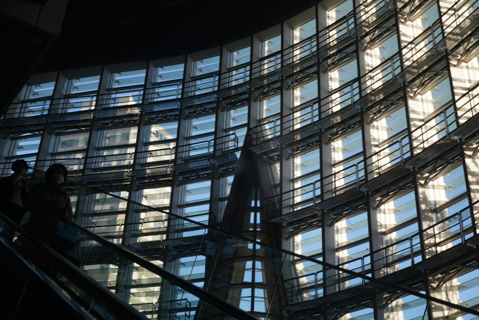 Vue intérieure d'un bâtiment avec des murs en verre et des personnes montant un escalier roulant