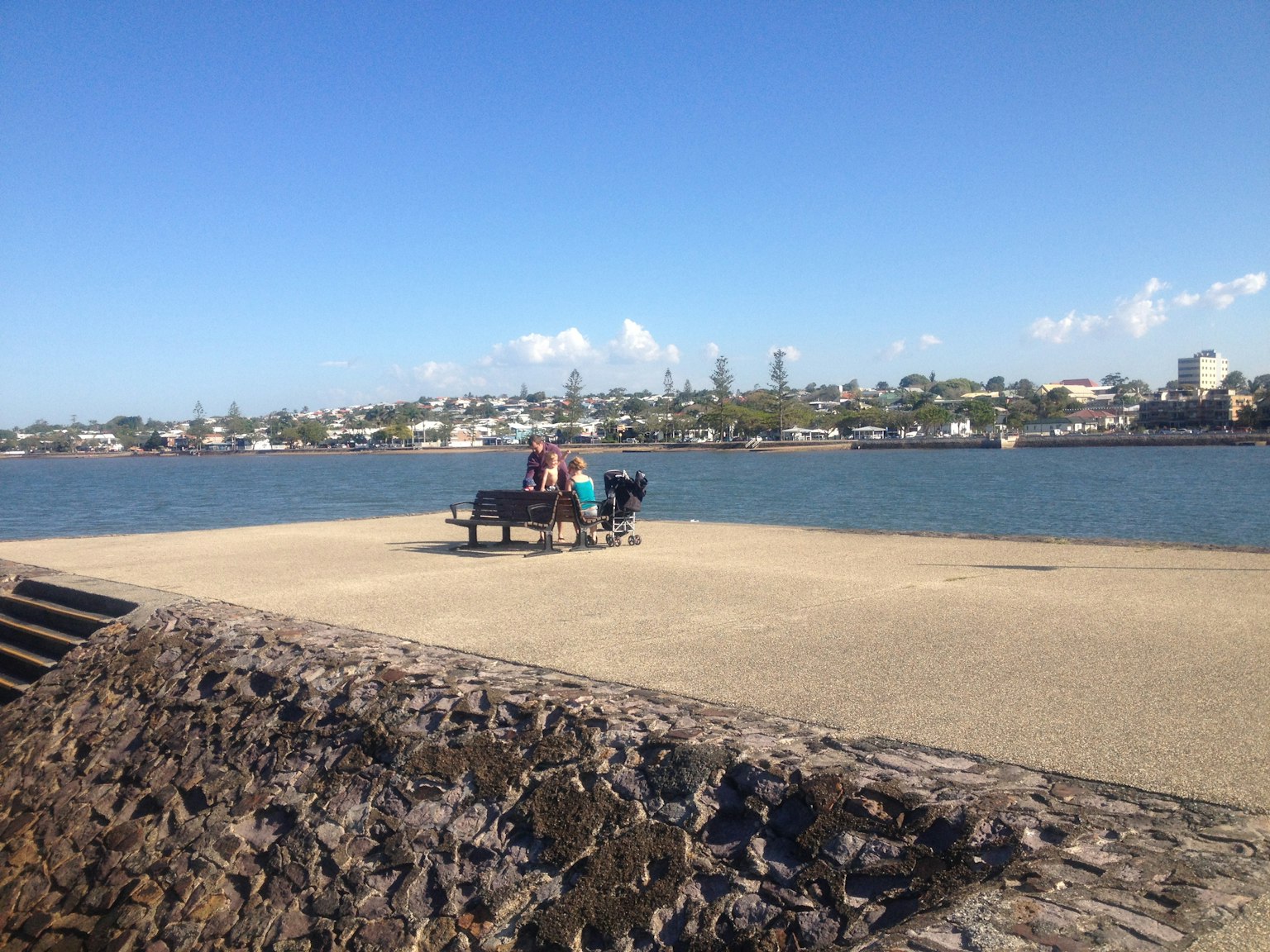 Des gens assis sur un banc au bord de l'eau avec une vue sur la ville