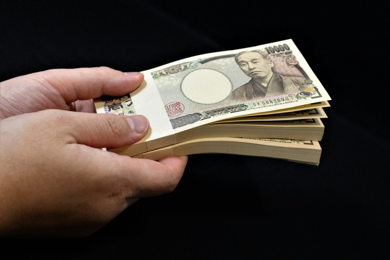 Una mazzetta di yen giapponesi tenuta in una mano visibile su uno sfondo nero