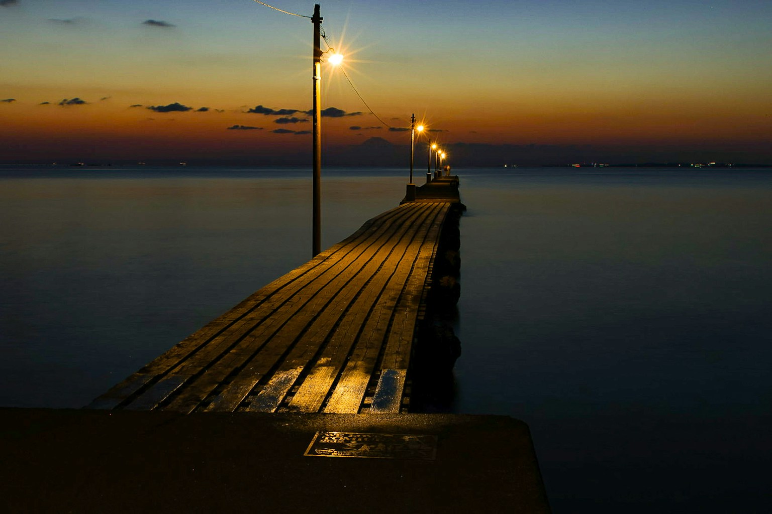 Vista panoramica di un molo che si estende nel mare crepuscolare con luci che illuminano le tavole di legno