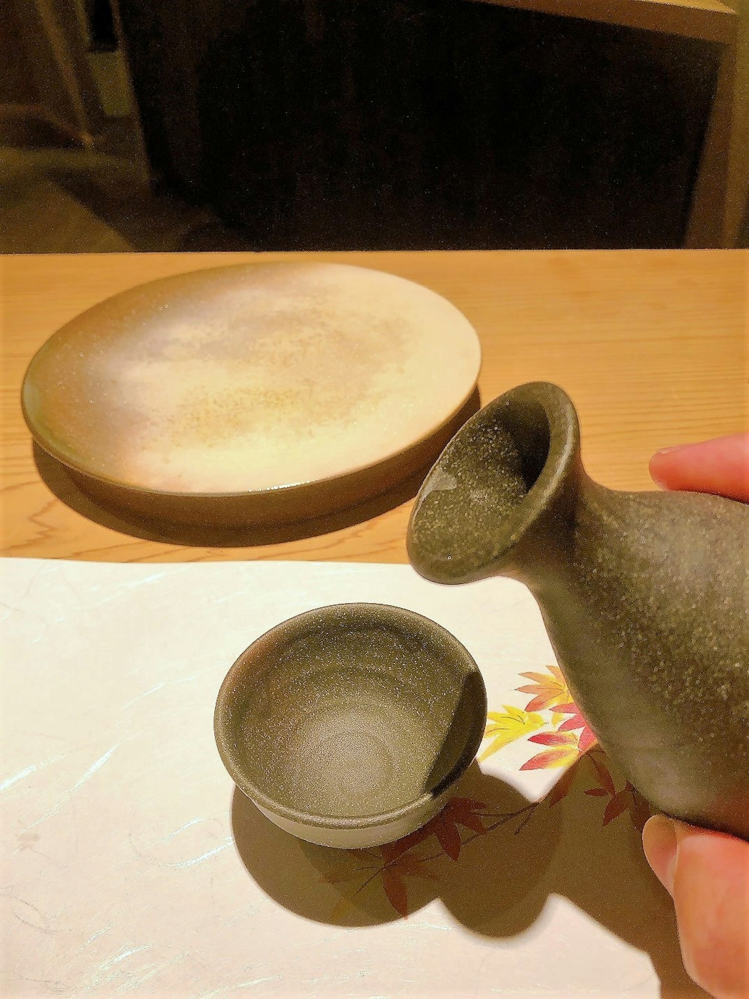Bottiglia di sake in ceramica grigia e piccola tazza tenuta in mano su un tavolo di legno