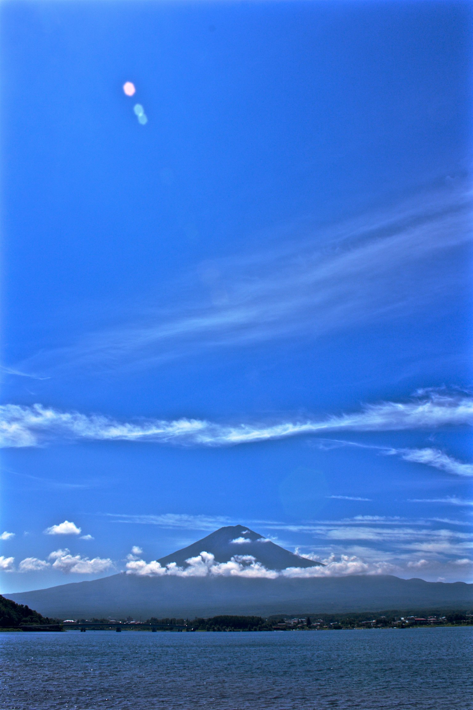 Mount Fuji rising under a blue sky with scattered clouds and a calm lake