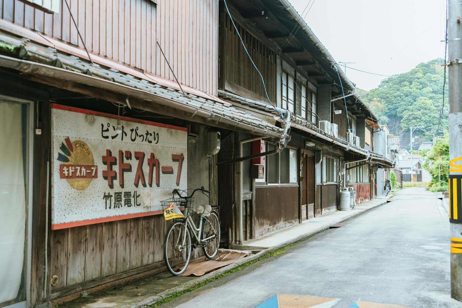 古い木造の建物が並ぶ静かな通り 自転車が置かれた看板が目立つ