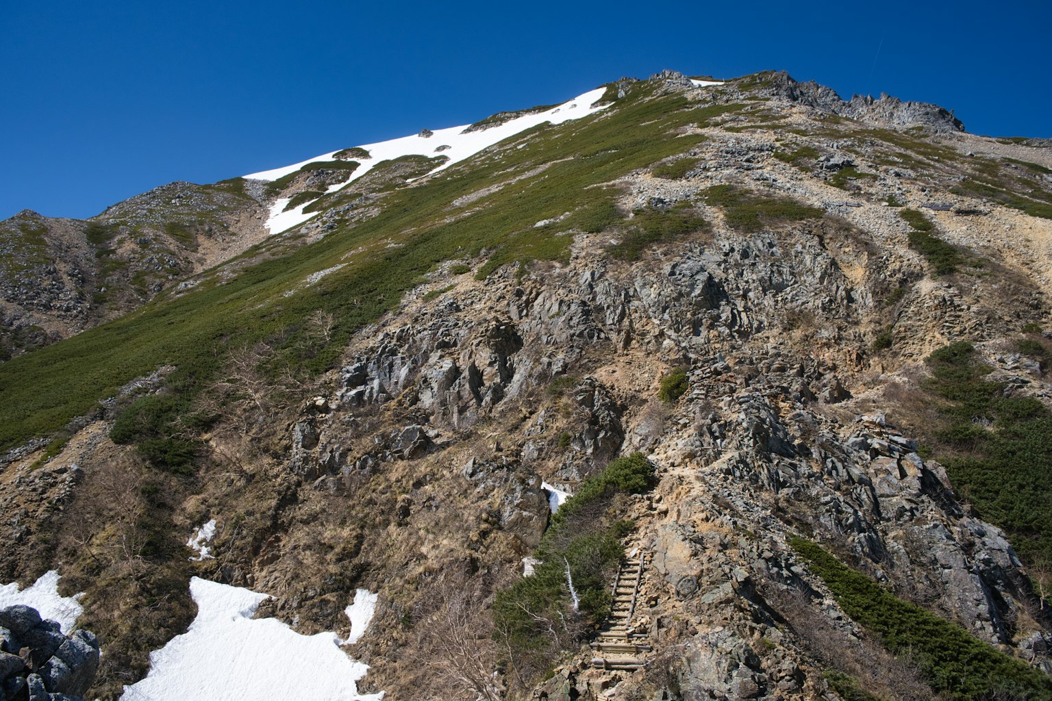 Bergneigung mit verbleibendem Schnee und grüner Vegetation unter einem klaren blauen Himmel