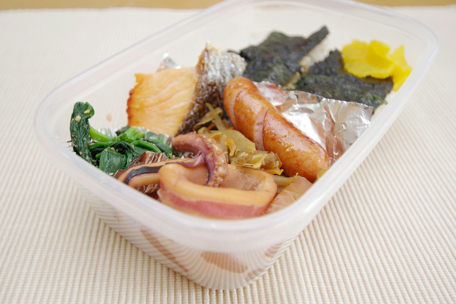 Bento japonais avec du poisson grillé, des algues et des légumes marinés dans un récipient transparent